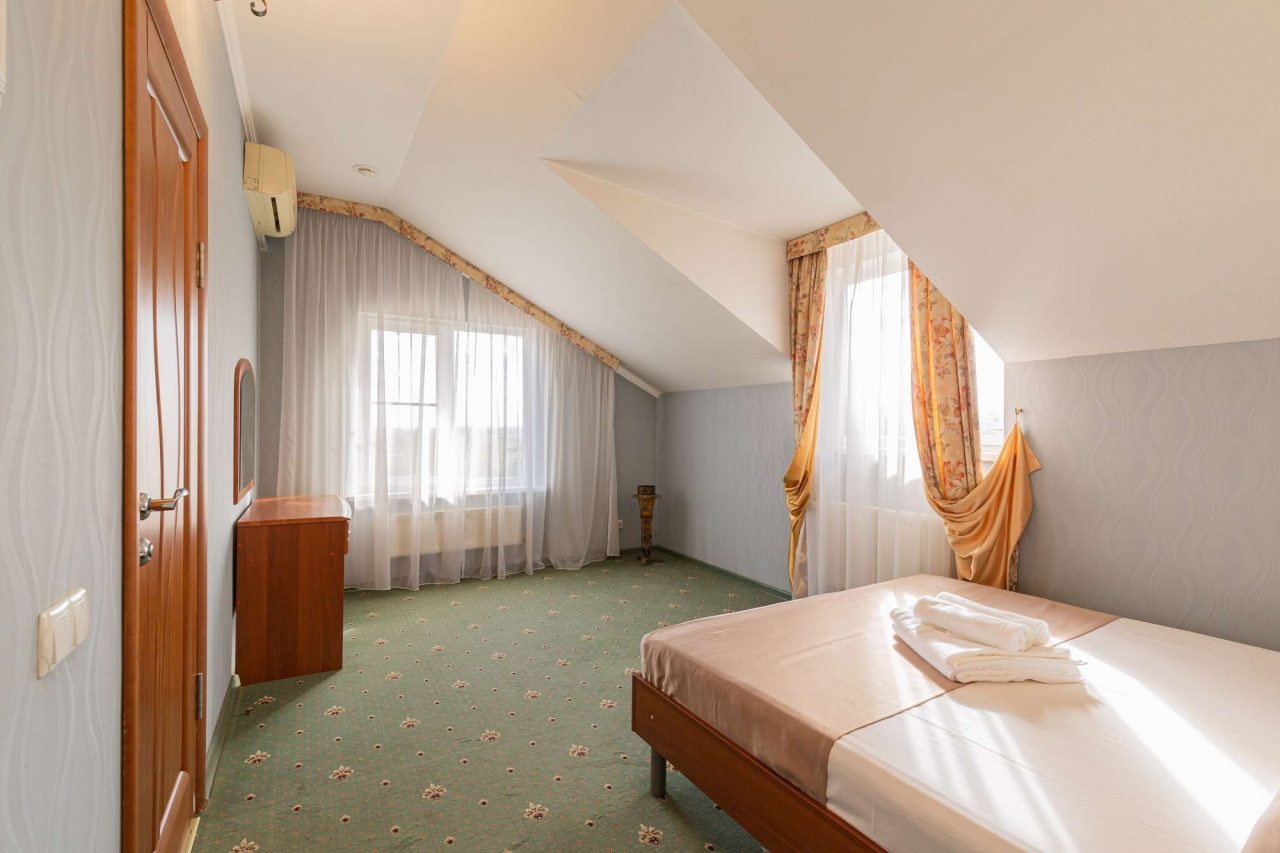 Двуспальная кровать покрыта бежевым покрывалом.